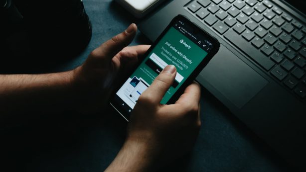 hands-hold-a-cellphone-showing-the-shopify-home-page